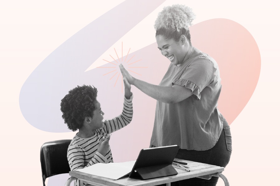 Elementary student sitting at desk with a laptop and high-fiving their teacher.